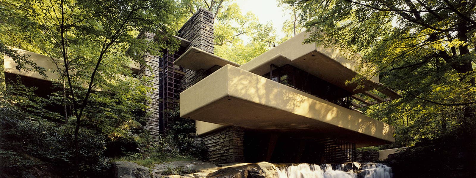 Fallingwater’s projecting concrete terraces and stone walls among trees above the waterfall.