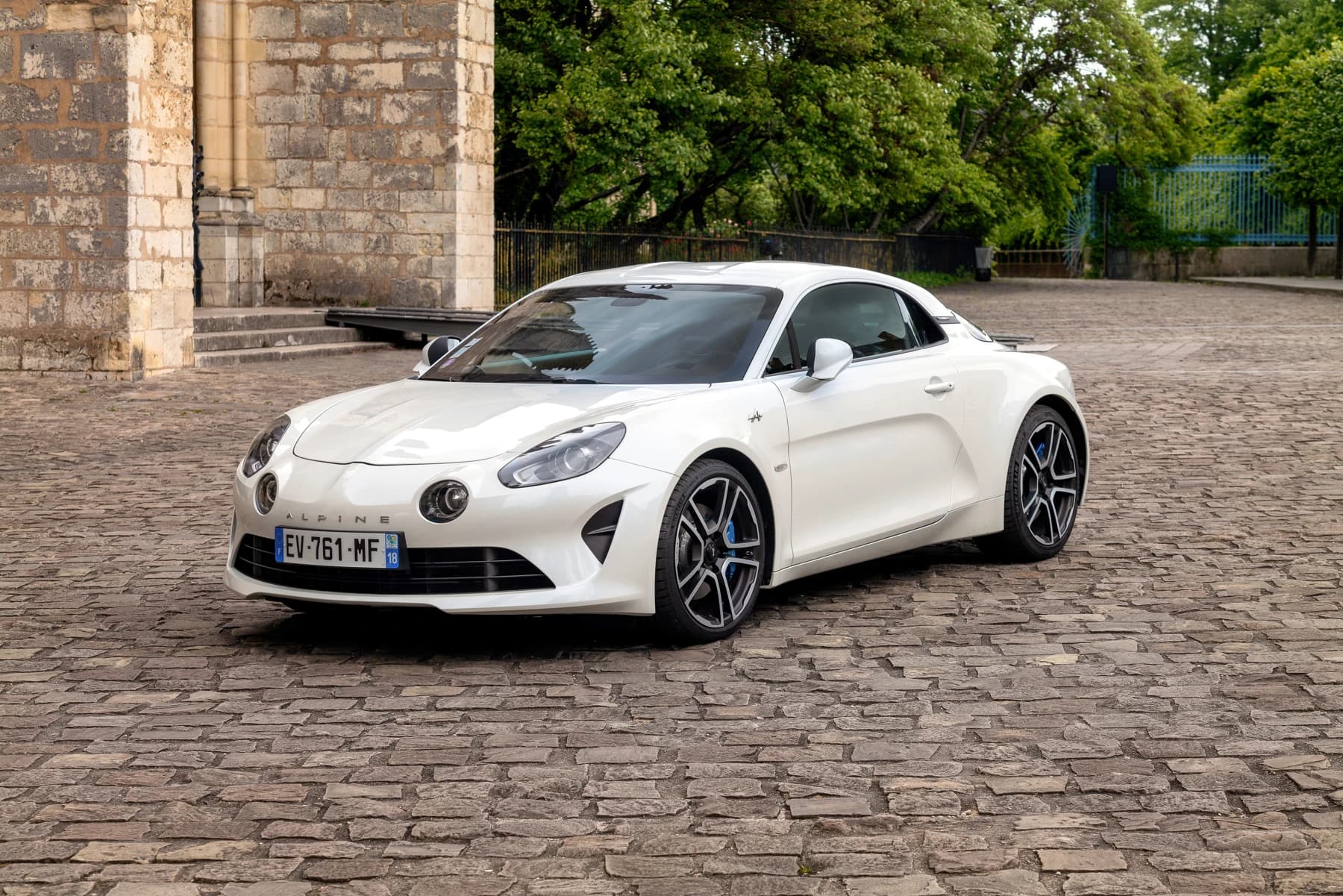 A white second-generation Alpine A110 Première Édition parked on a cobbled street in Bourges, with its low body, round front lamps and wheels visible.