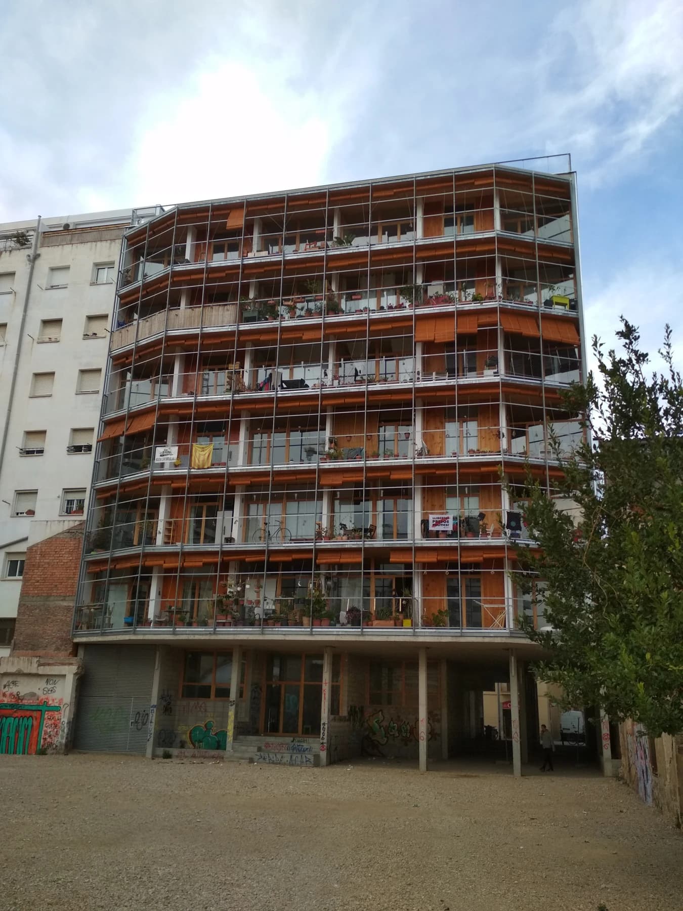 The rear elevation of La Borda cooperative housing in Barcelona, with stacked timber balconies, red structural elements and planting across the inhabited building.