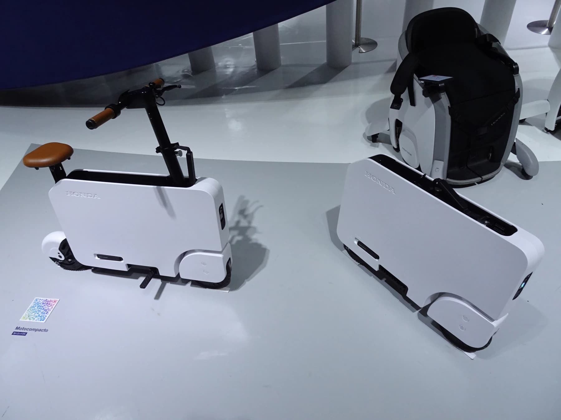 Honda Motocompacto scooters displayed folded into a white rectangle and unfolded for riding at the Japan Mobility Show, making both configurations visible together.