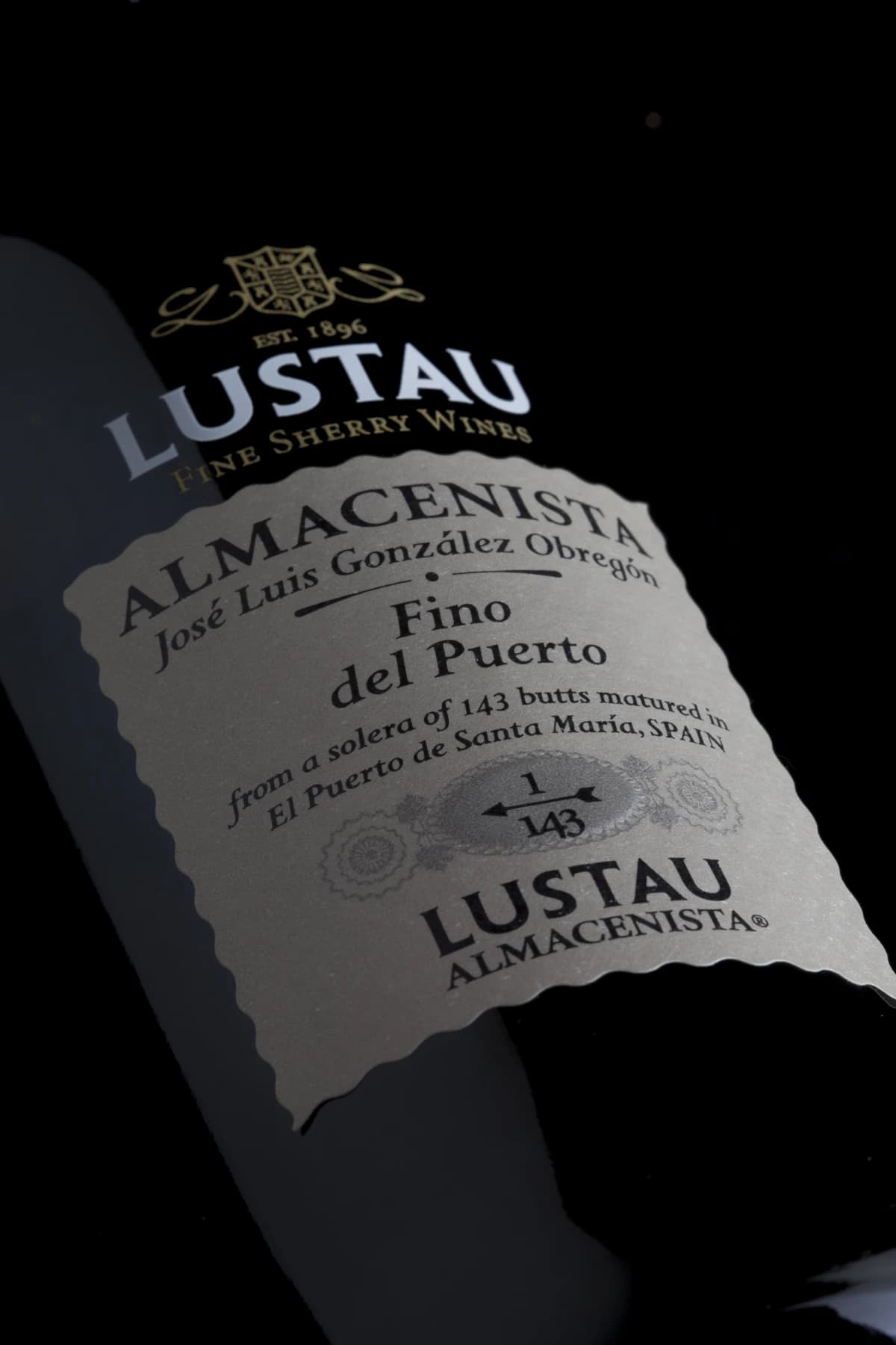 A close, diagonally composed photograph of a Lustau Almacenista Fino del Puerto bottle, with the González Obregón name and 1/143 solera marking visible on the label.