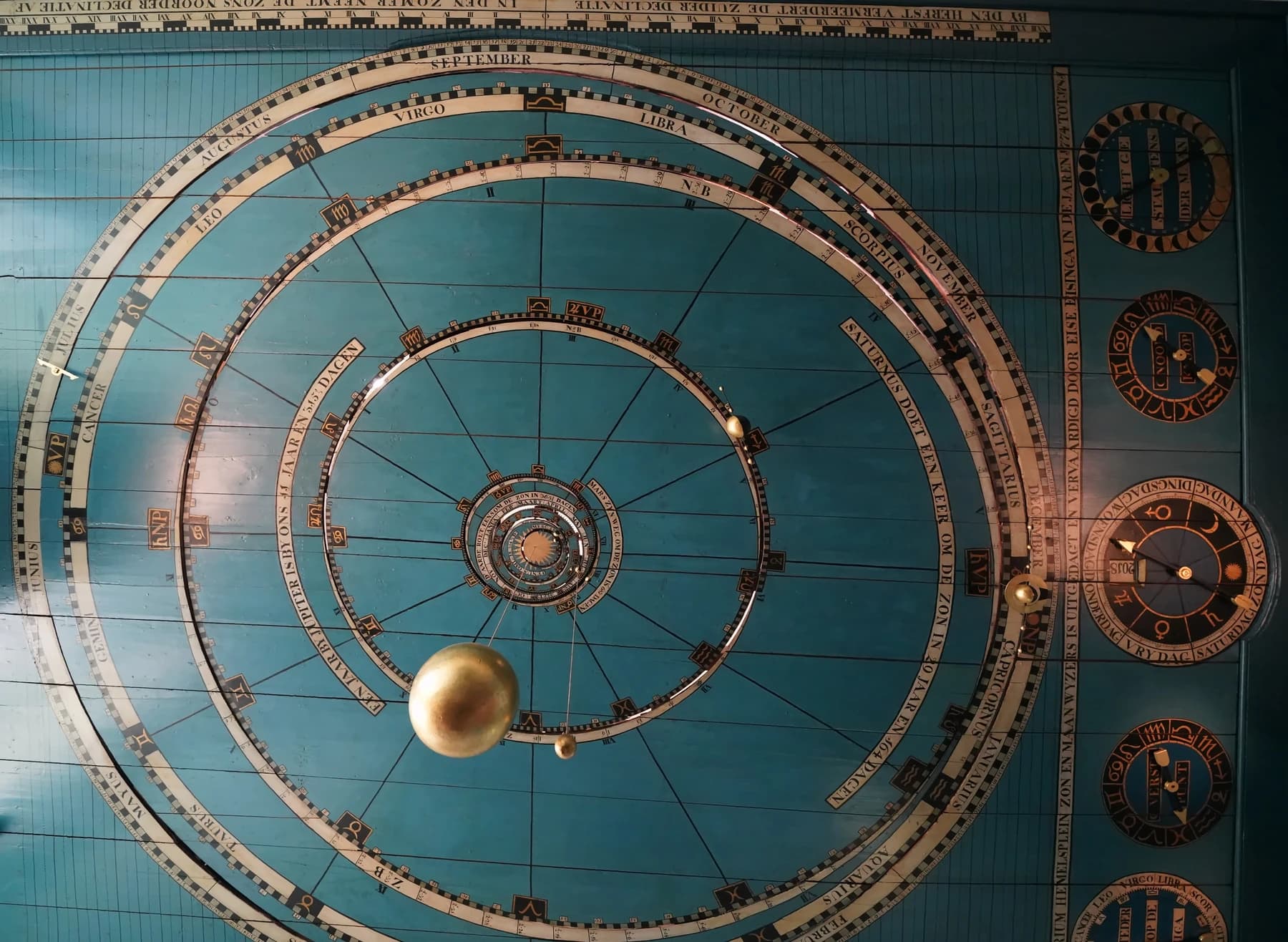 The blue ceiling of Eise Eisinga’s planetarium in Franeker, showing circular gold orbital tracks, a suspended golden Sun, small planetary spheres and calendar dials.