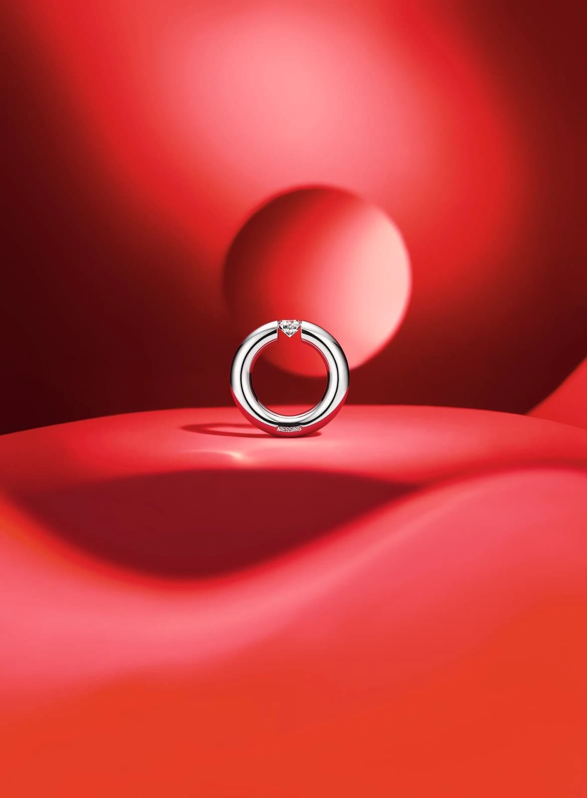 A platinum Niessing Spannring Round standing upright on a red sculptural surface, with its tension-held diamond visible at the gap in the circular band.