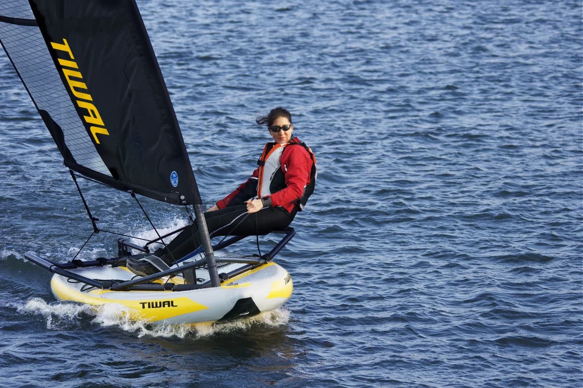 Marion Excoffon sailing an early Tiwal 3.2 inflatable dinghy, sitting on the side frame in a red jacket above its white and yellow hull on blue water.