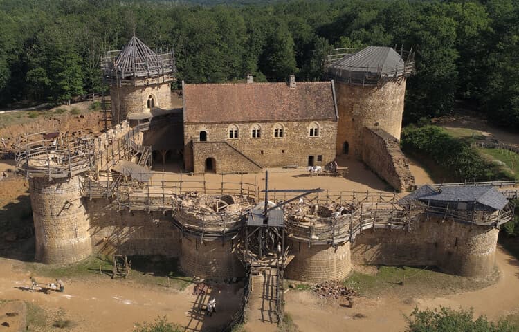 Aerial view of Guédelon’s stone castle, towers and active construction site within woodland.
