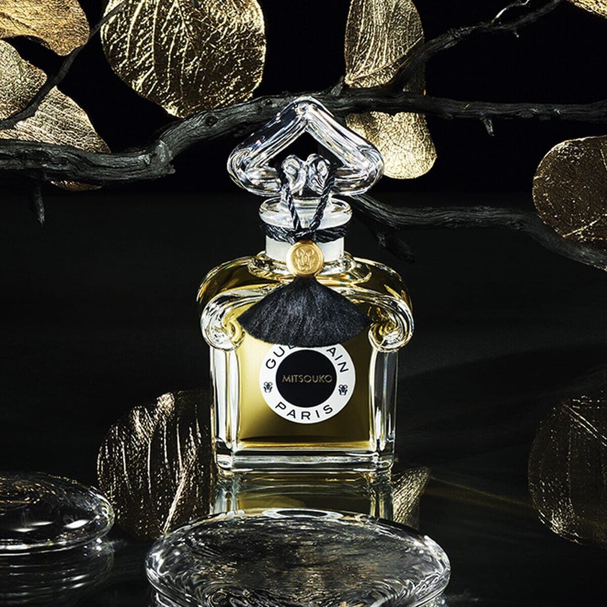 A contemporary bottle of Guerlain Mitsouko set among black branches, gold leaves and glass pebbles.
