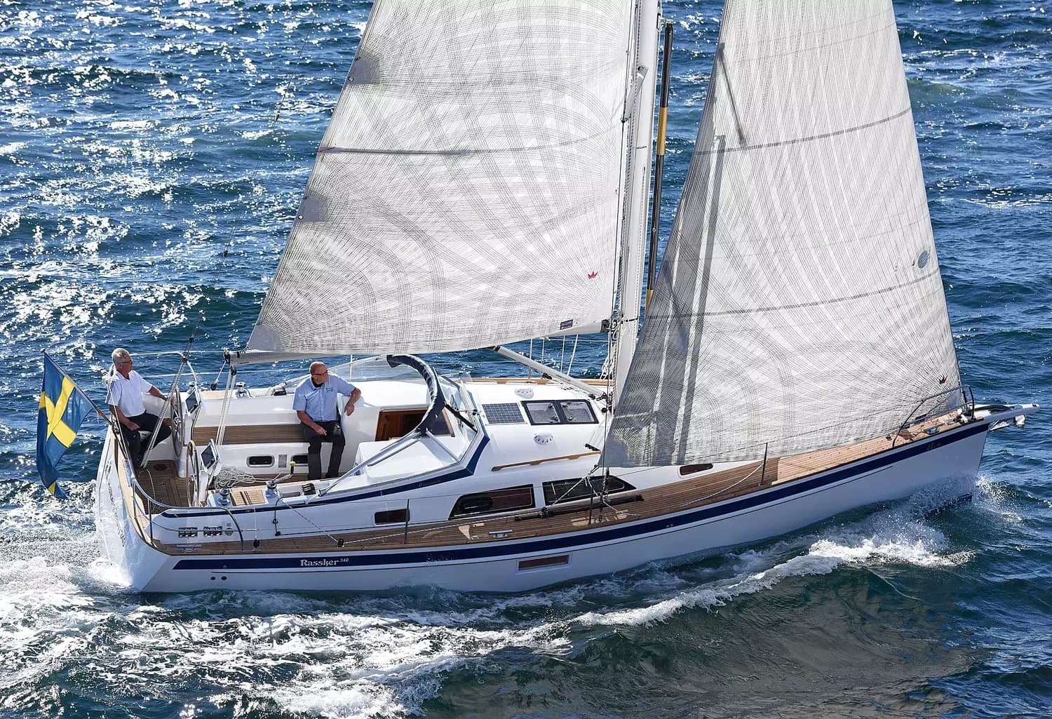A Hallberg-Rassy 340 sailing from an elevated view, with two people in the cockpit and white sails drawing.