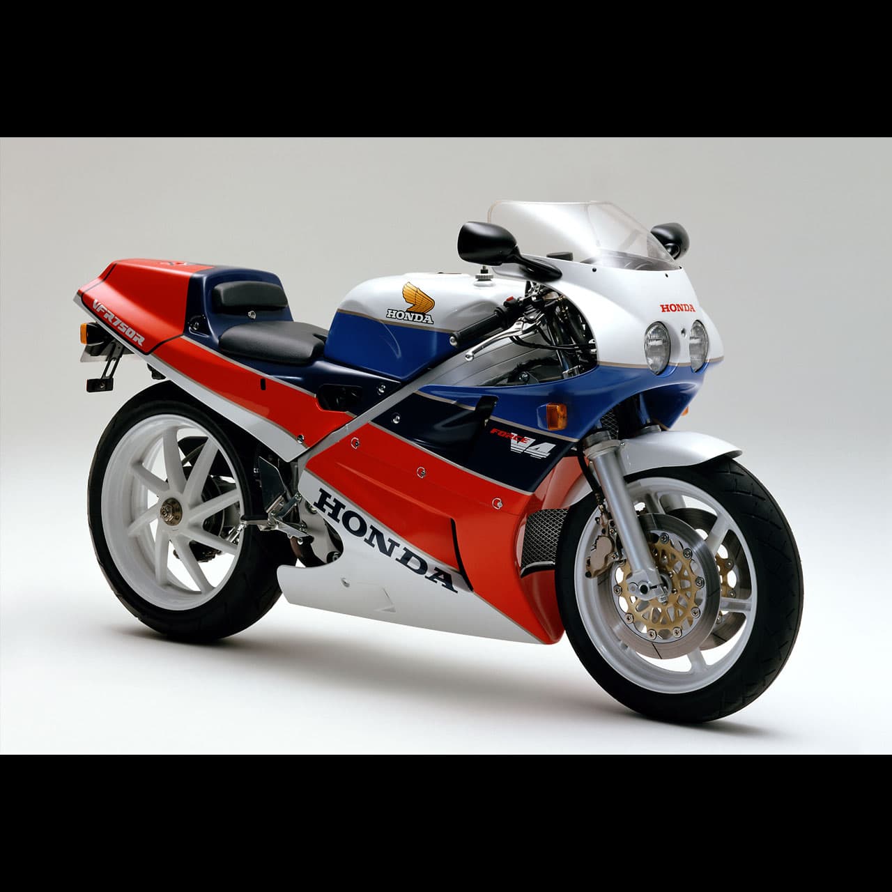 Honda VFR750R RC30 in white, red and blue, shown in a three-quarter studio view.