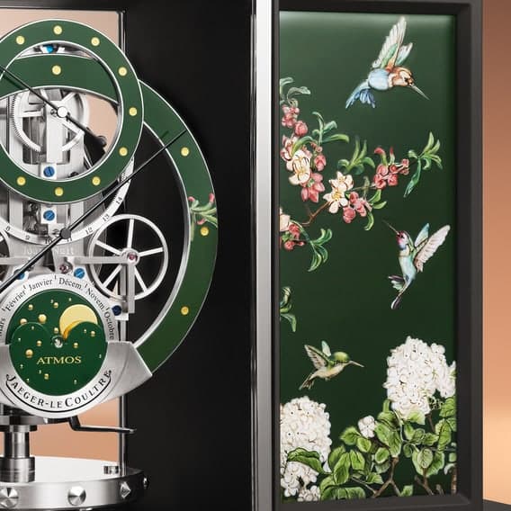 Detail of a Jaeger-LeCoultre Atmos clock beside a green enamel panel painted with hummingbirds and flowers.