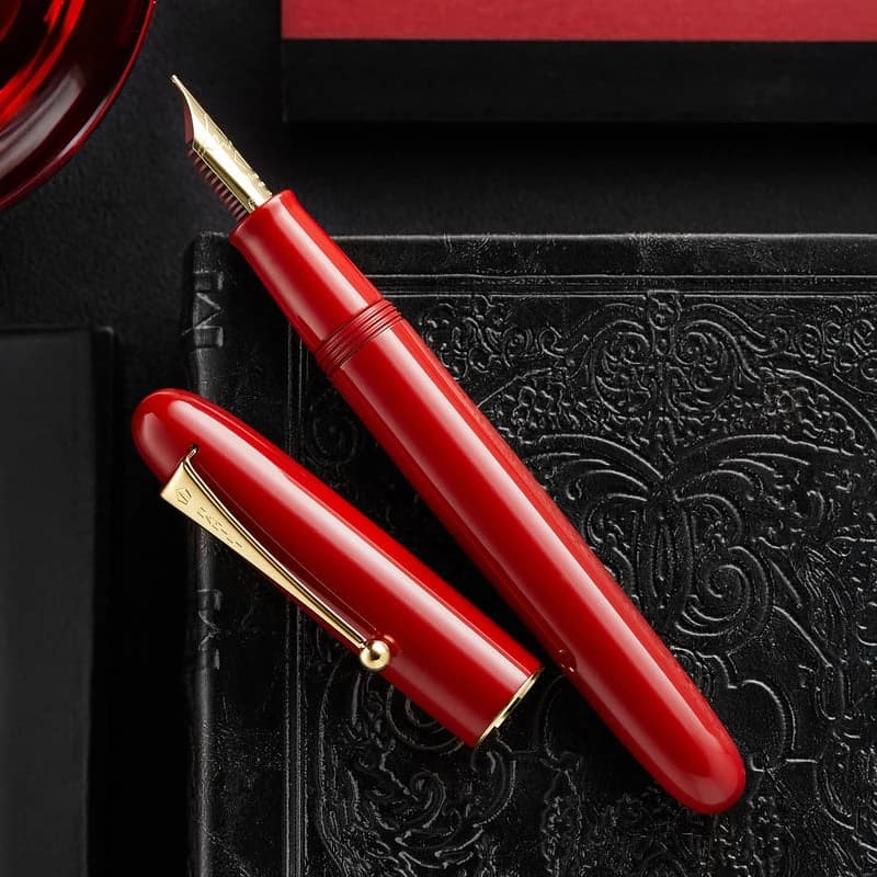 A vermilion Namiki Yukari Royale Urushi fountain pen and cap on a dark textured surface.