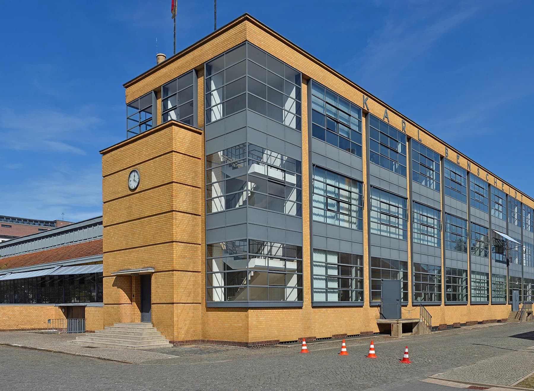 The Fagus factory’s brick and glass main building in Alfeld, with its glazed corner and tall gridded windows beneath a blue sky.