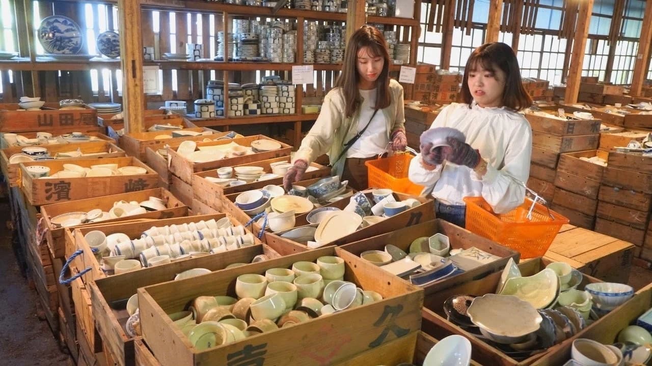 Two visitors holding baskets while looking through shelves of porcelain in the Kouraku Kiln warehouse in Arita.