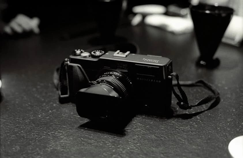 A Hasselblad XPan film camera resting on a bar in a monochrome photograph, with its broad body and attached lens visible.