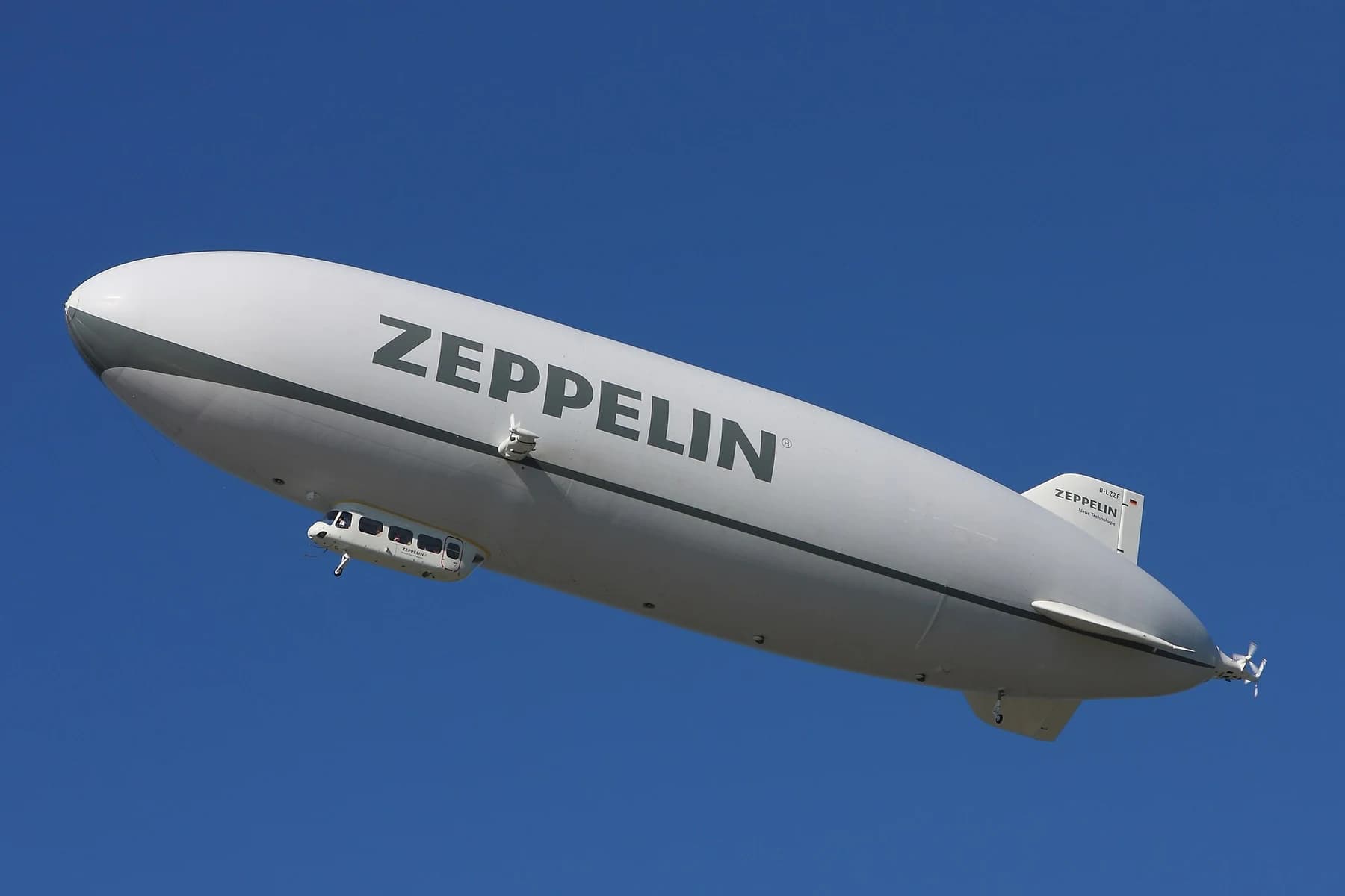 A white Zeppelin NT airship with its cabin and tail fins clearly visible against a deep blue sky.