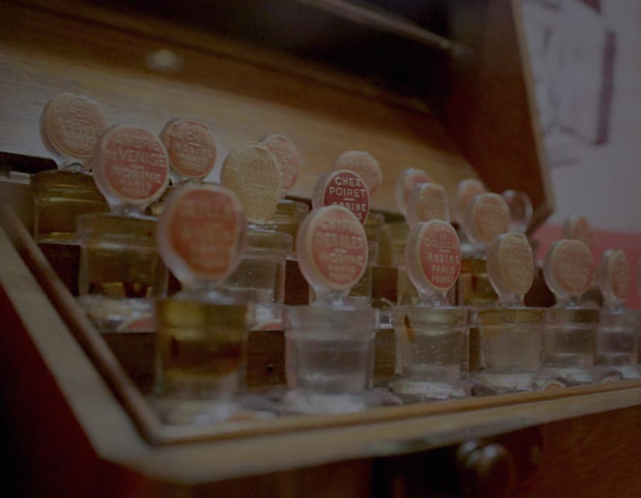 Rows of small historic perfume bottles with handwritten and printed labels inside an archival case.