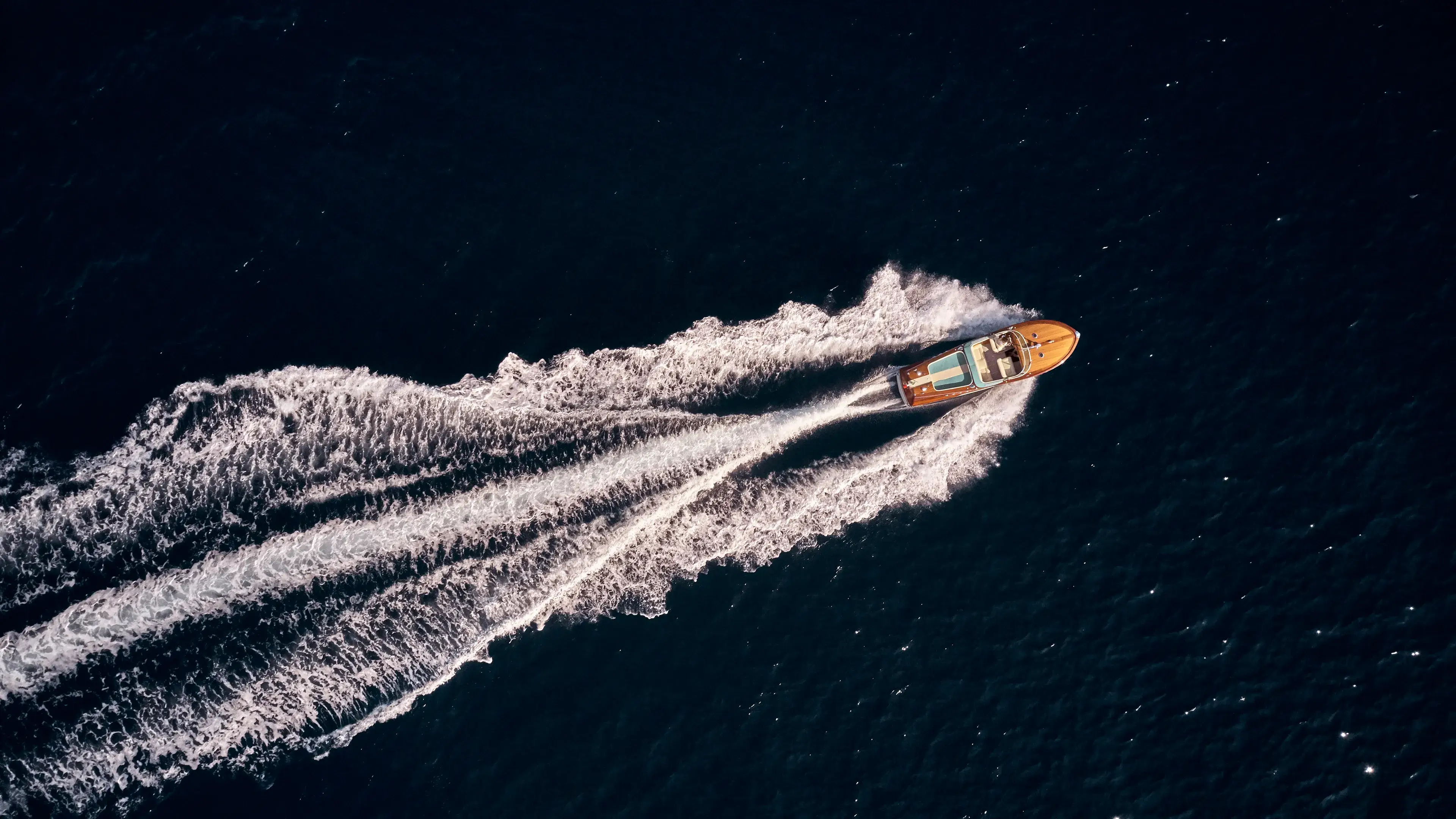 A classic wooden Riva runabout seen from above on deep blue water.