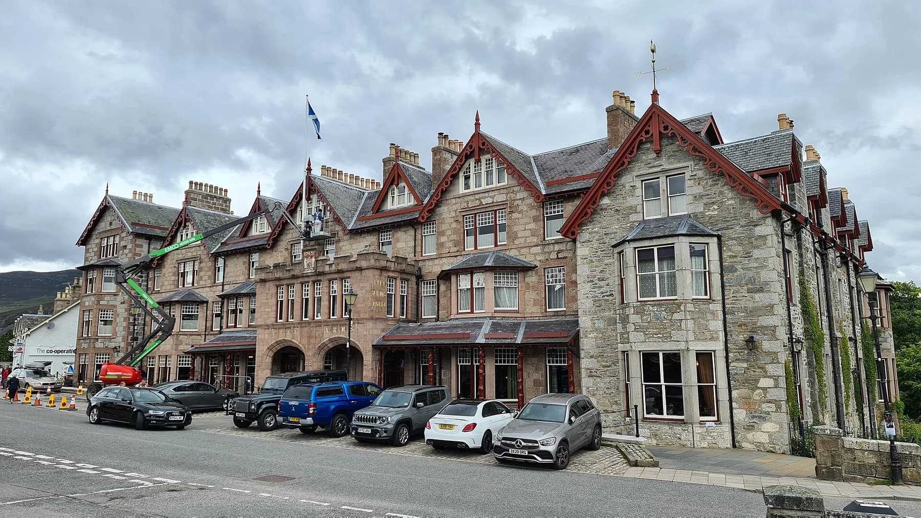 The complete stone frontage of the Fife Arms hotel in Braemar, with red-trimmed gables, bay windows and parked cars along the village street.