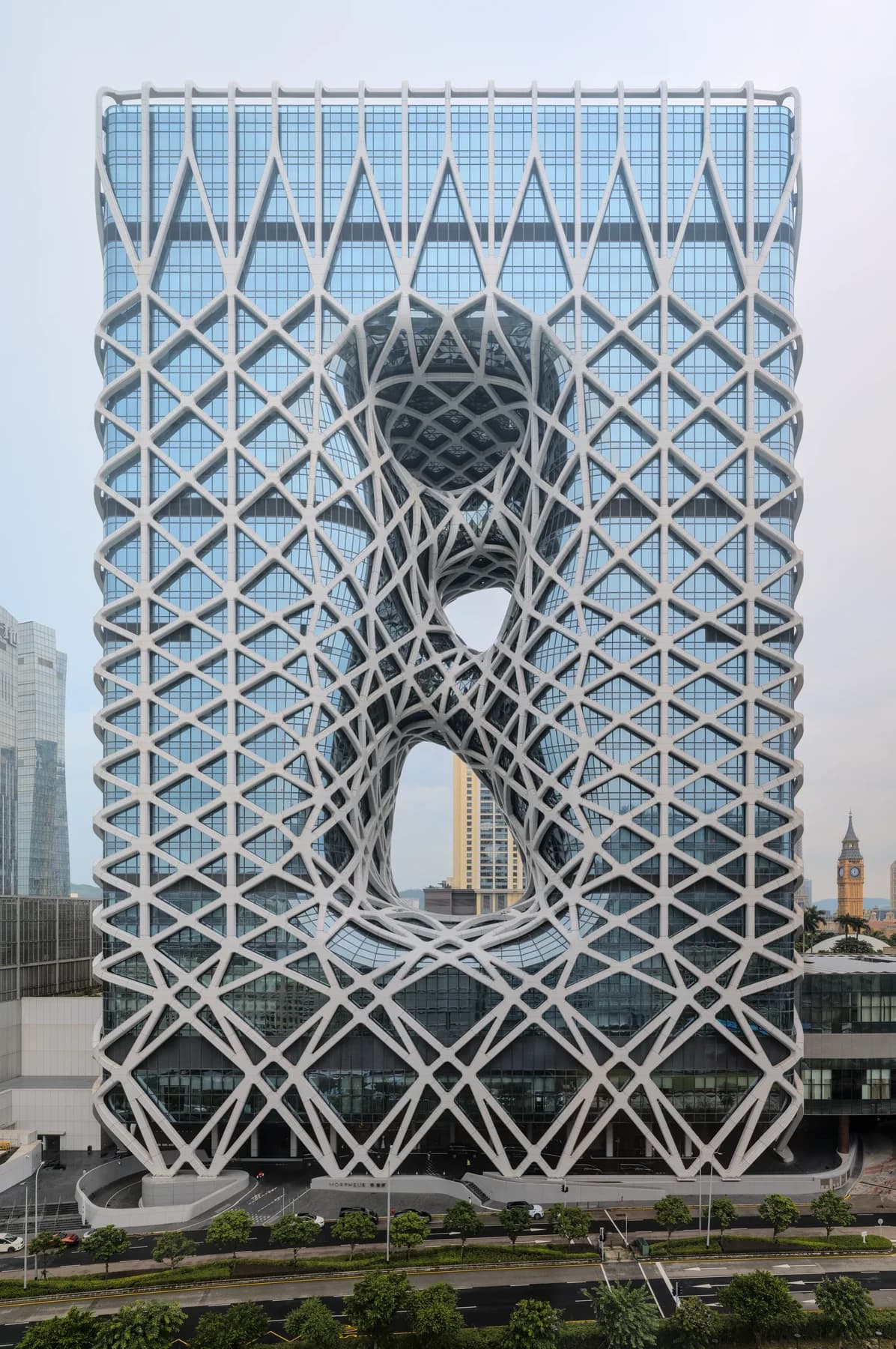 The complete Morpheus hotel tower in Macau, with a pale external lattice surrounding large openings through its dark glazed body.
