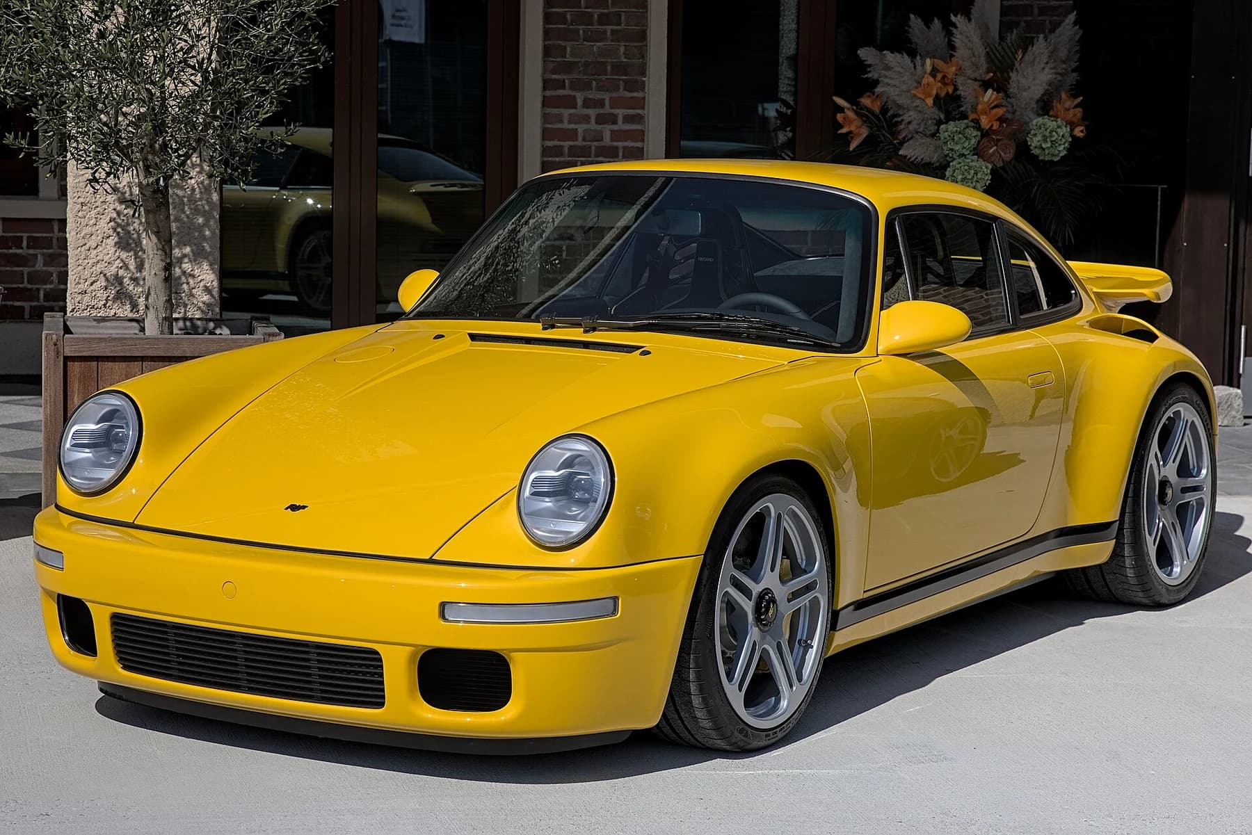 A yellow RUF CTR Anniversary seen from the front quarter at Motorworld Munich, with a compact body, round lamps and a rear wing.