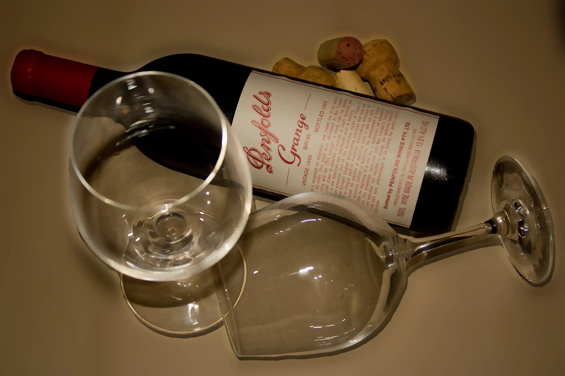 An archival 1992 Penfolds Grange bottle lying diagonally beside two wine glasses and corks, with the vintage and Bin 95 label visible.