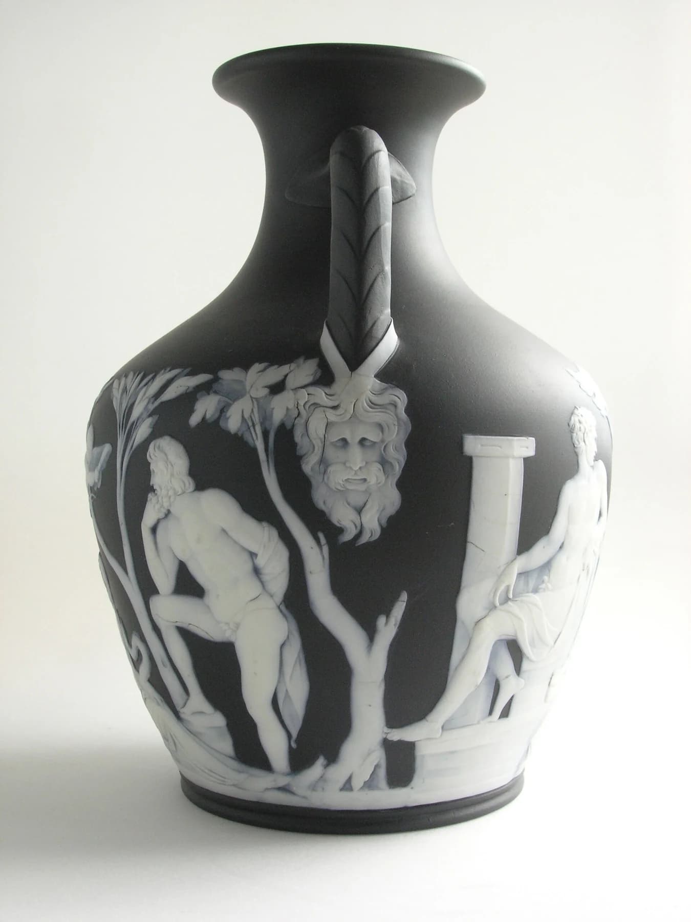 A dark Wedgwood Portland Vase copy from Auckland Museum with pale classical figures in relief, curled handles and a flared neck on a neutral background.