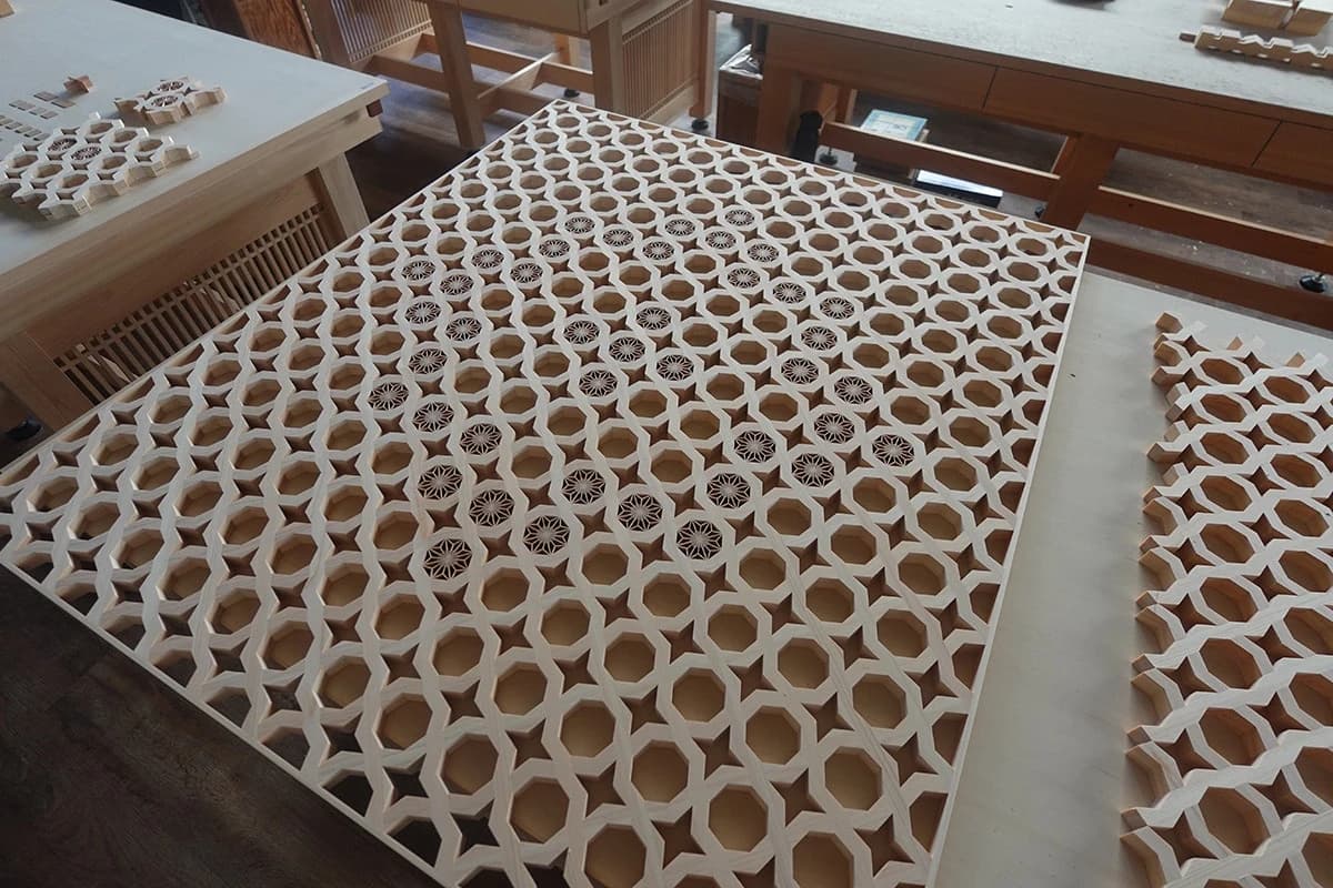 A pale wooden lattice panel with repeated geometric openings on a workshop table, reproduced with Tanihata’s kumiko and mangour collaboration announcement.