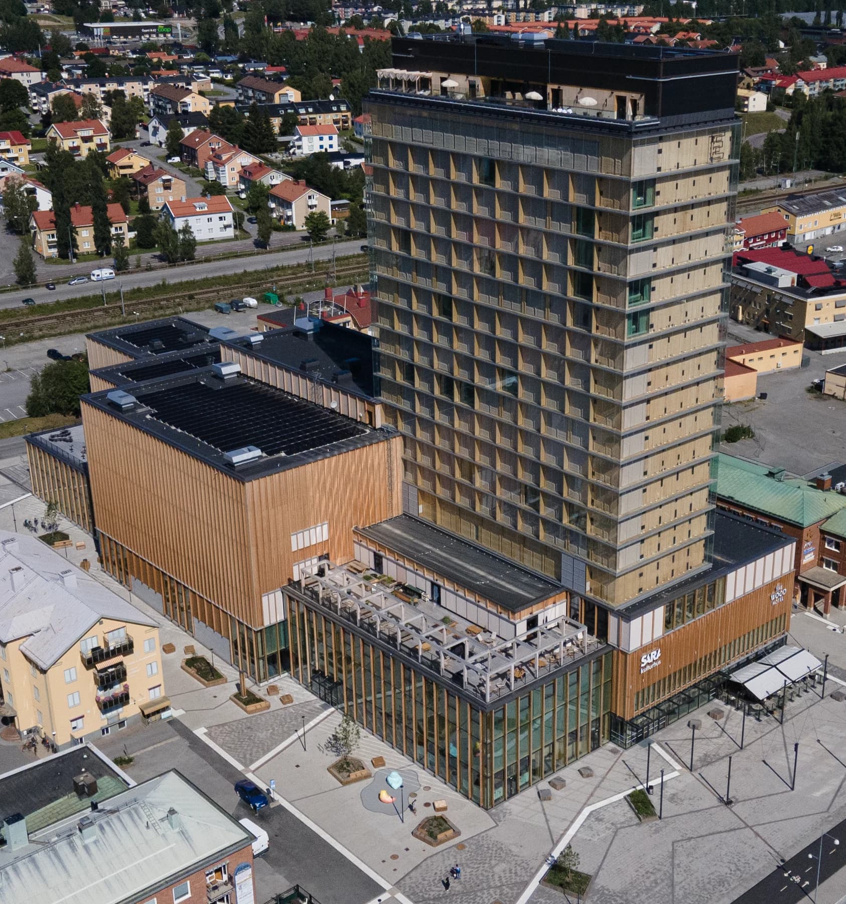 Sara Kulturhus in Skellefteå seen from above in summer, with the tall glass-clad hotel tower rising over the broad timber cultural building and its square.