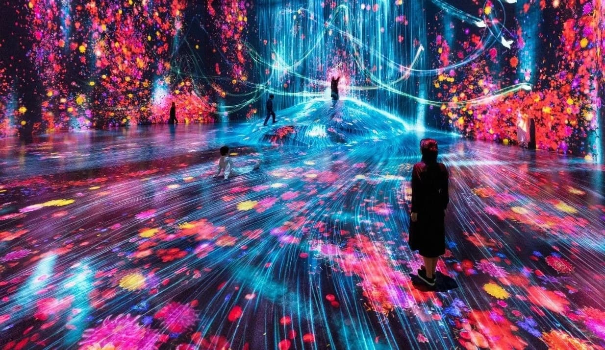 Visitors among vivid flowers and flowing blue and red light in a teamLab Borderless installation at Azabudai Hills in Tokyo.