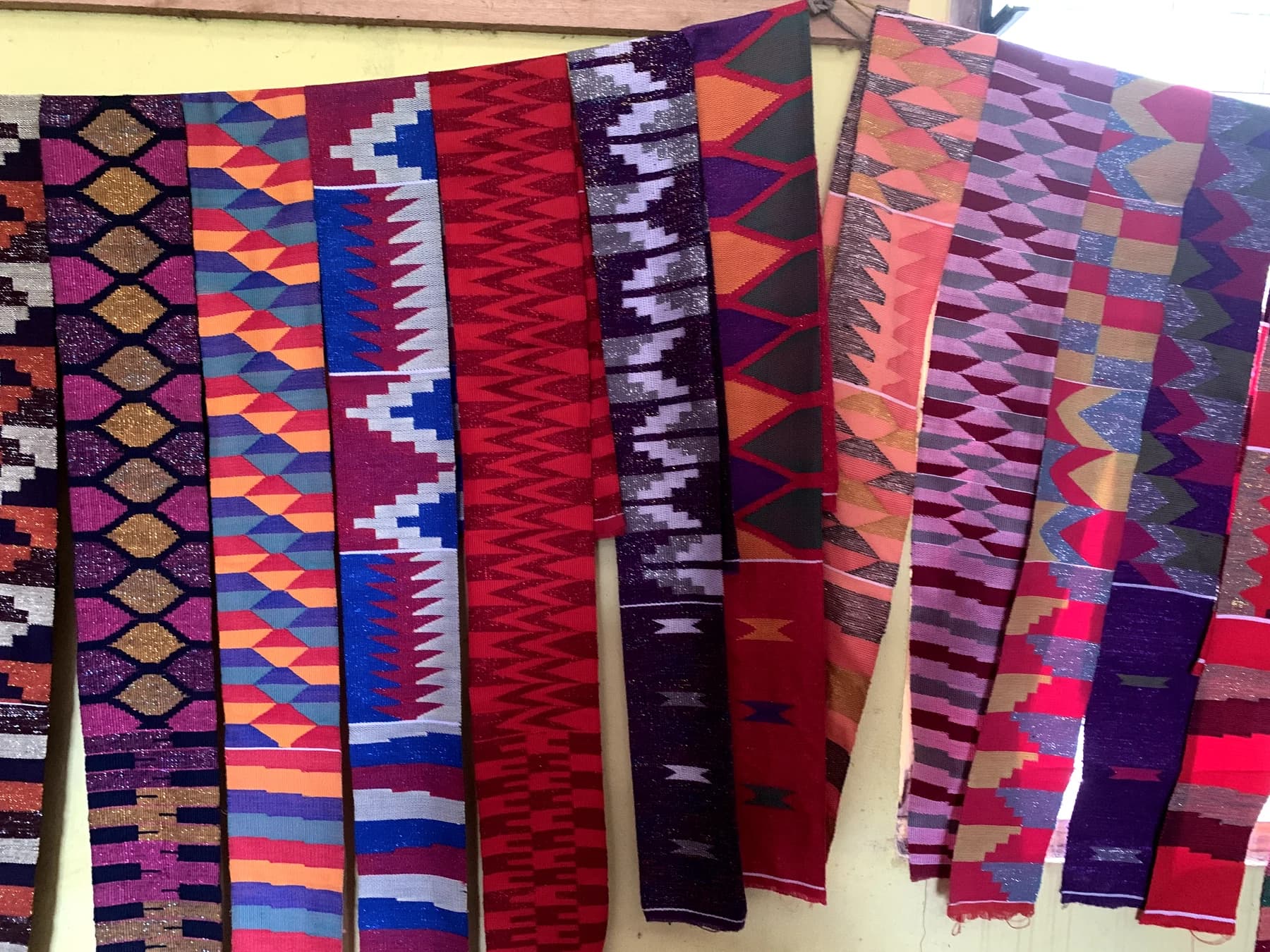 Long textiles with vivid red, violet, orange and blue geometric patterns hang side by side at Tafi weaving village.