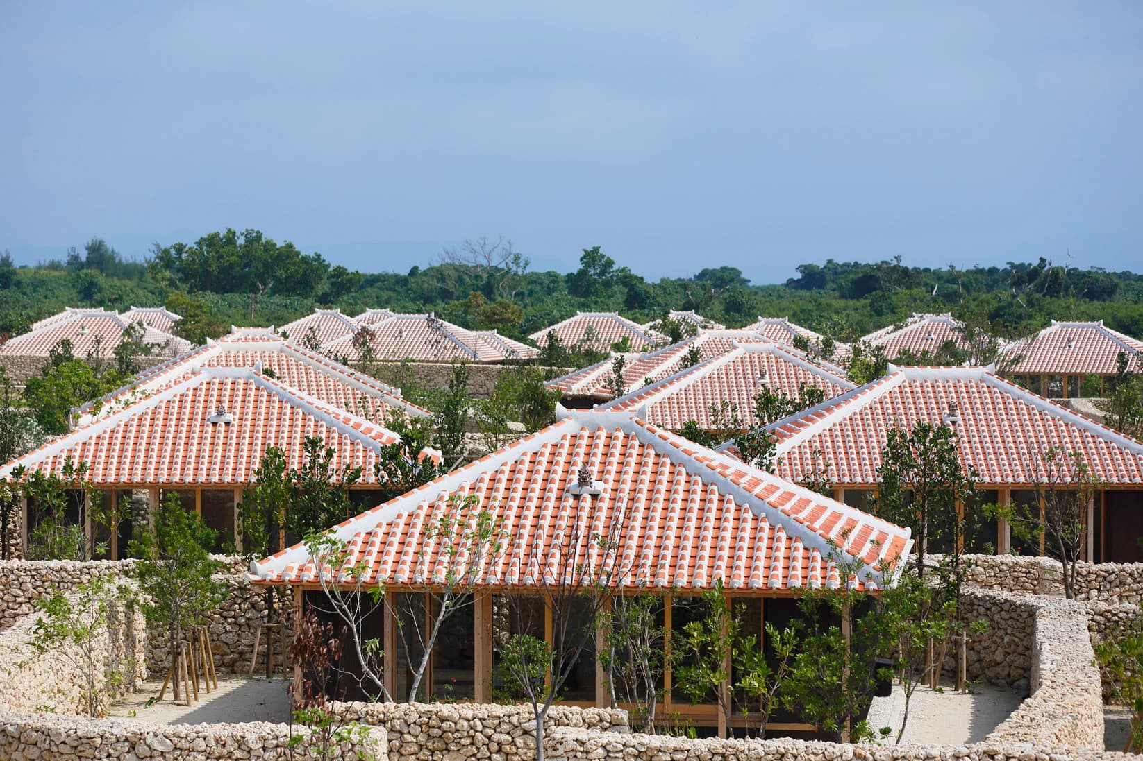 Low red-tiled villa roofs, limestone walls and planted courtyards form a village-like arrangement beneath a blue sky on Taketomi Island.