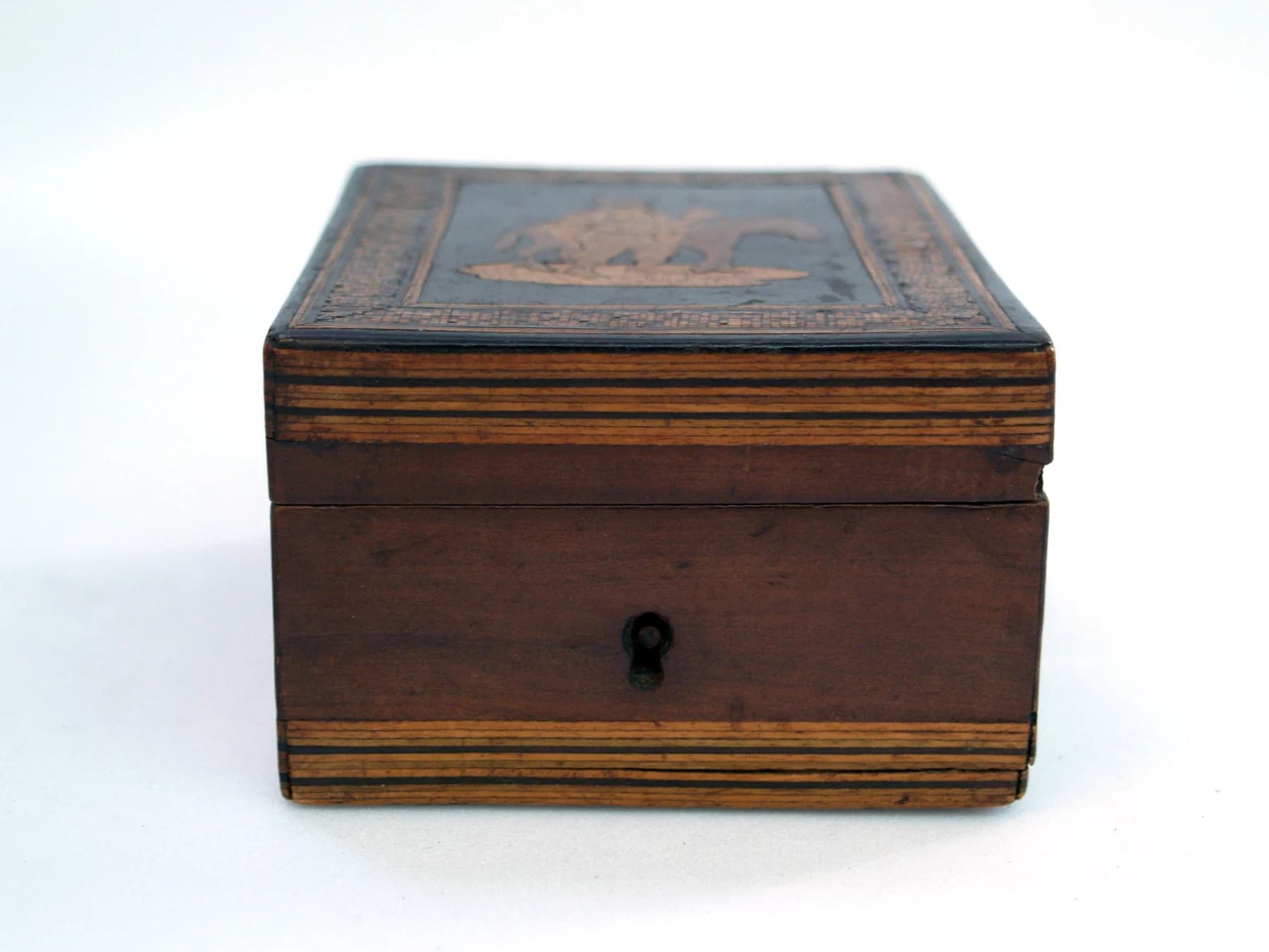 A small dark wooden box with a keyhole, fine mosaic borders and an inlaid scene of a rider on a donkey on its closed lid.