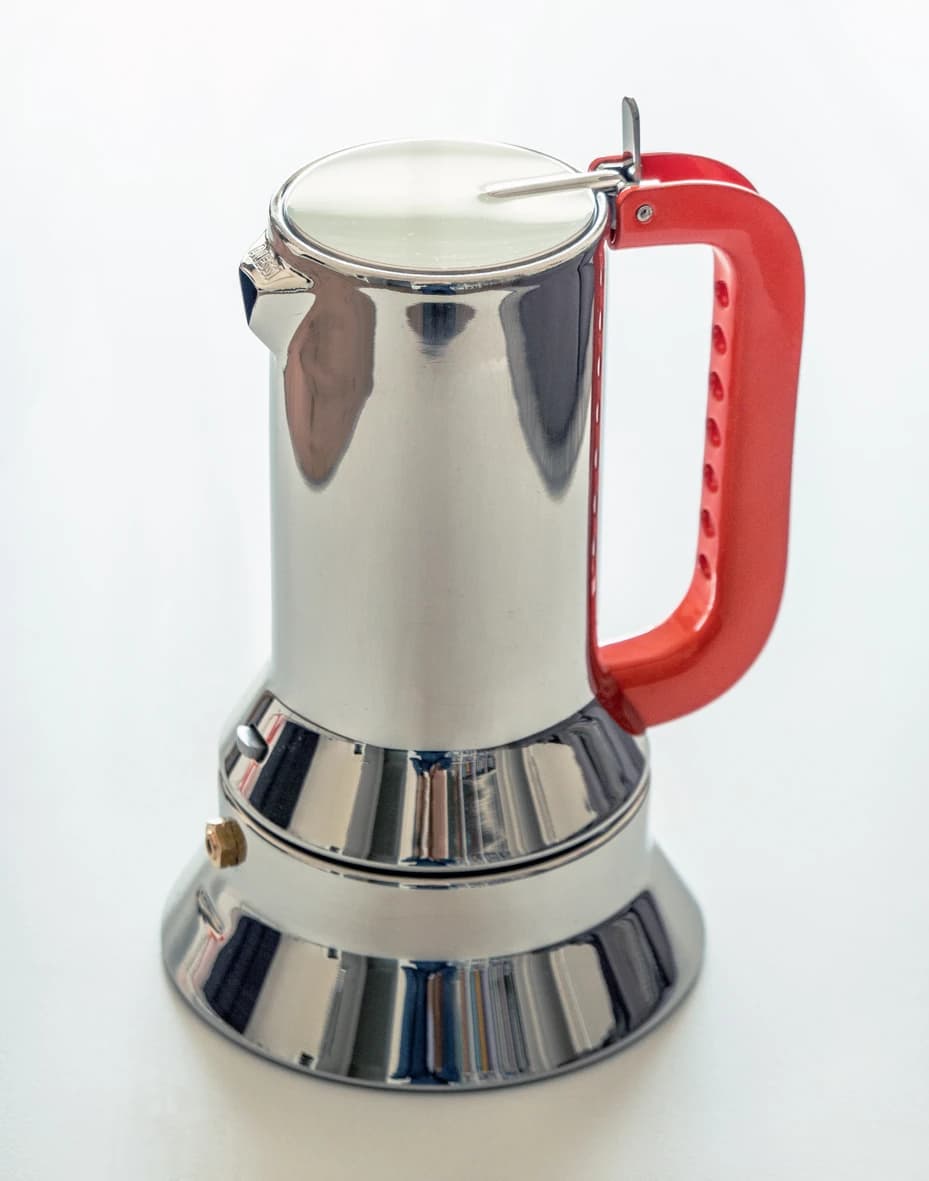 An Alessi 9090 stovetop coffee maker with polished steel body and a red lever handle, photographed against a light background.