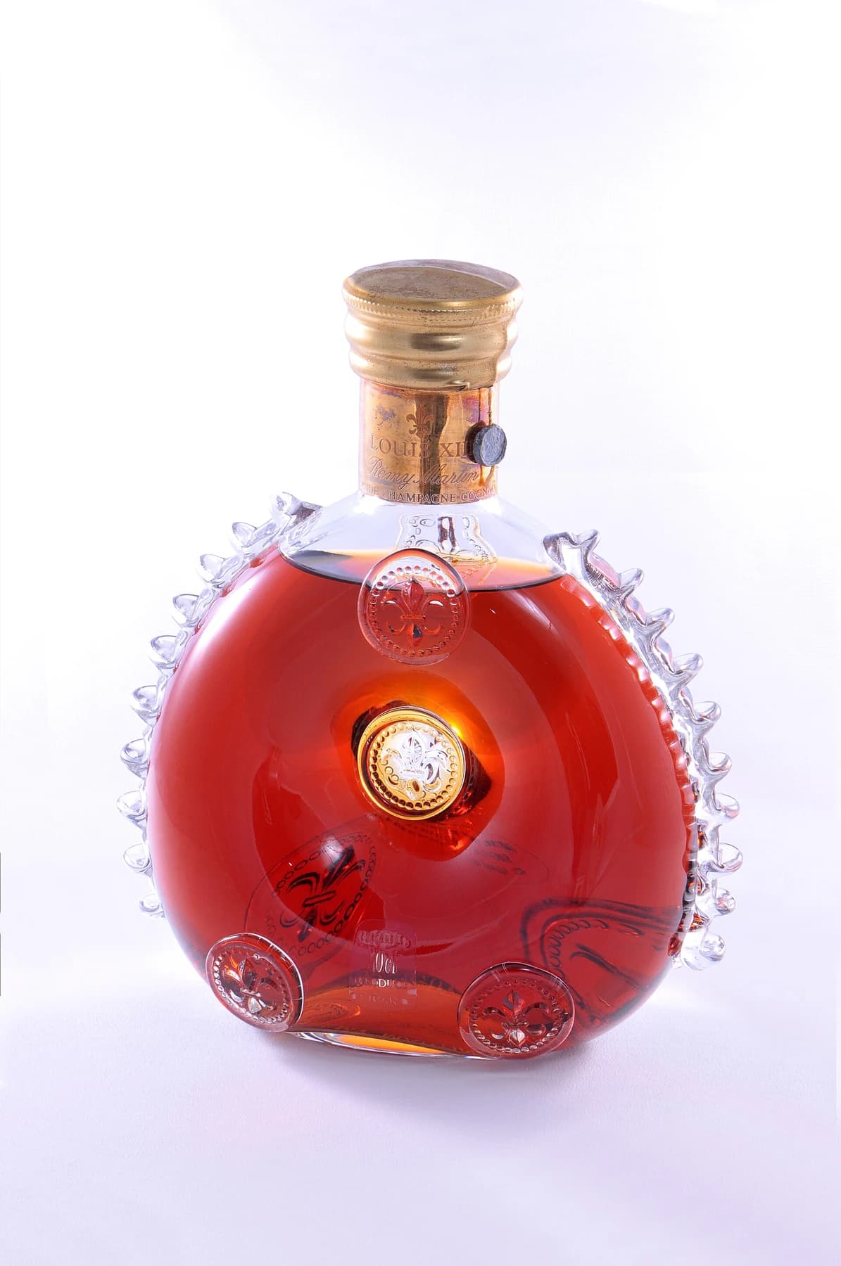 A Louis XIII de Rémy Martin cognac decanter on a pale background, showing its amber liquid, decorative glass edges and stopper.