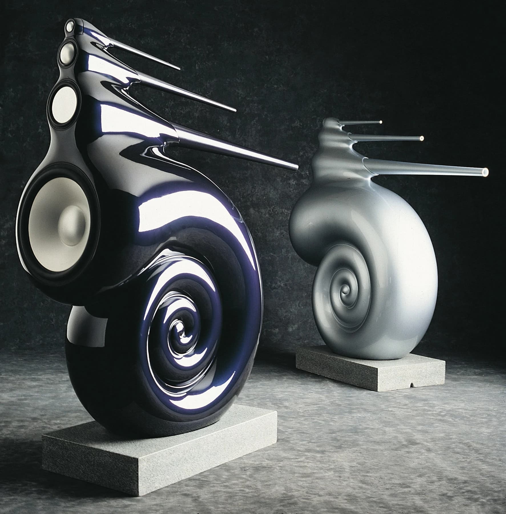 A pair of Bowers & Wilkins Nautilus loudspeakers with coiled bass enclosures and projecting tapered tubes, photographed against a dark background.