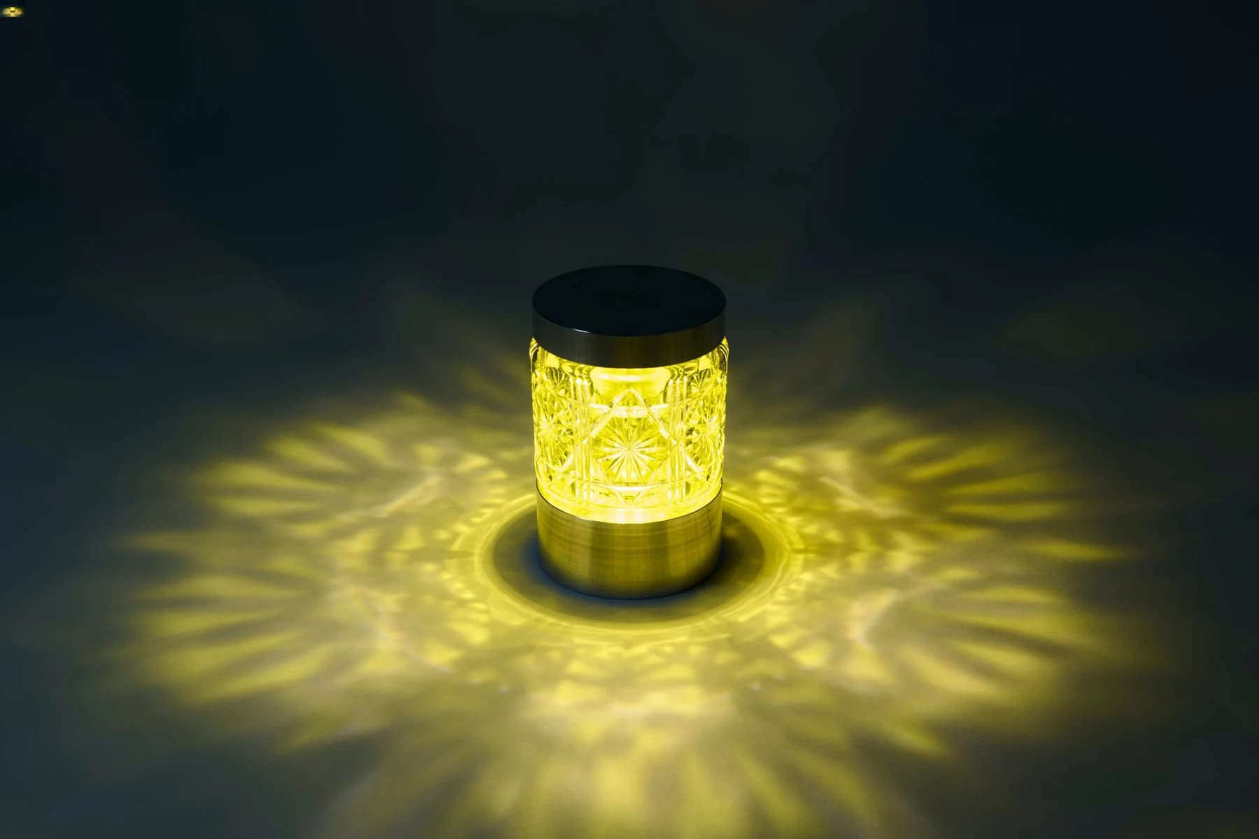 The TOKIMEKI and Shimadzu Satsuma Kiriko lighting object glowing in yellow glass, casting a radial pattern across a dark tabletop from its cut surface.
