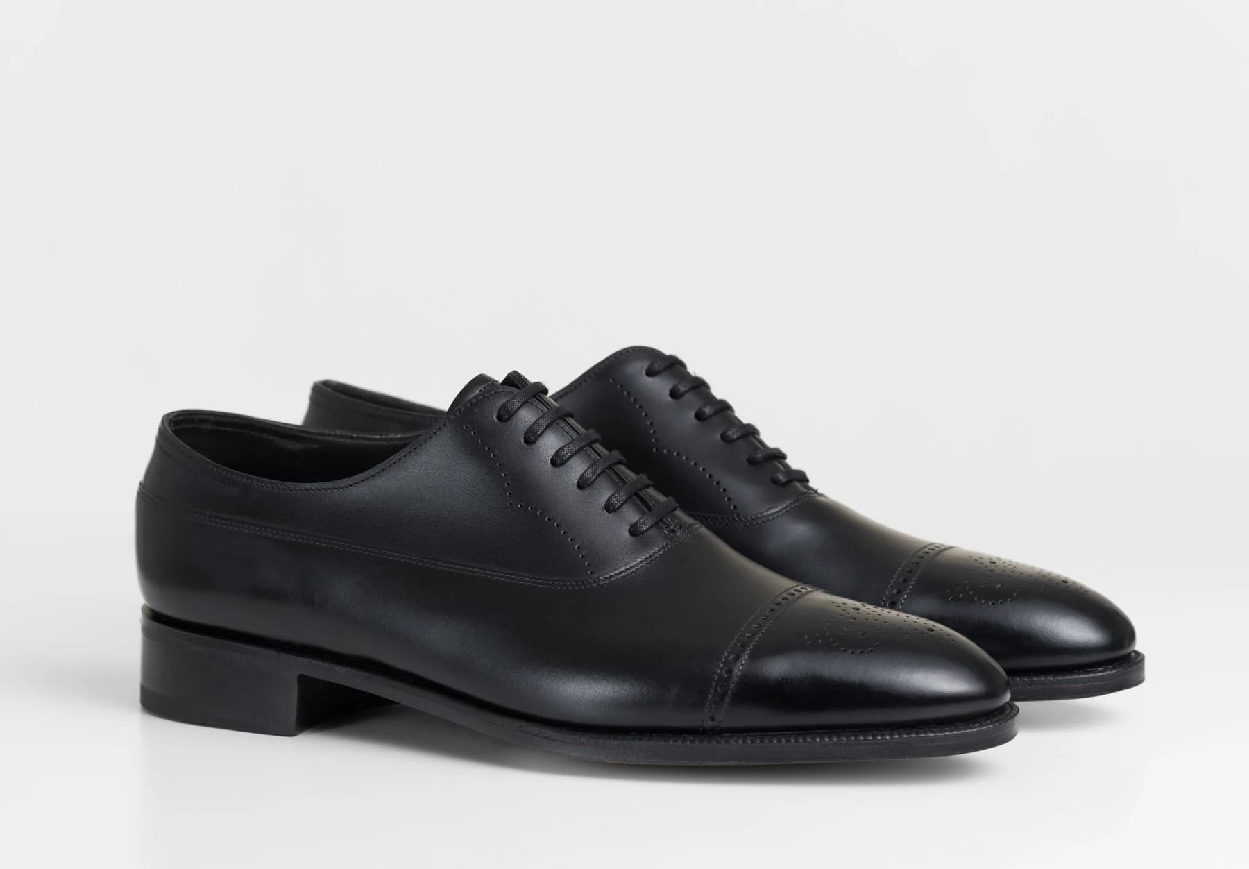 A pair of black John Lobb Lazenby semi-brogue shoes on a white background, showing the laced uppers, perforated detailing and leather soles.