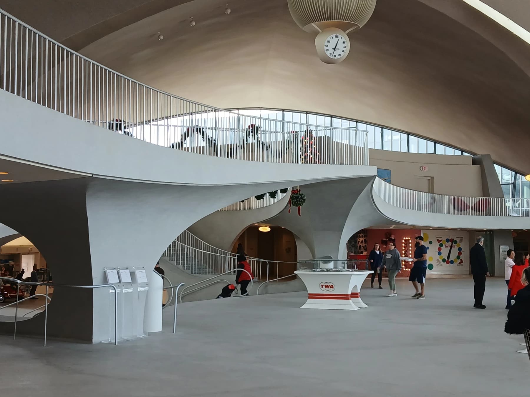 The restored TWA Flight Center interior with sweeping white concrete curves, a balcony edge and large windows bringing daylight into the historic headhouse.
