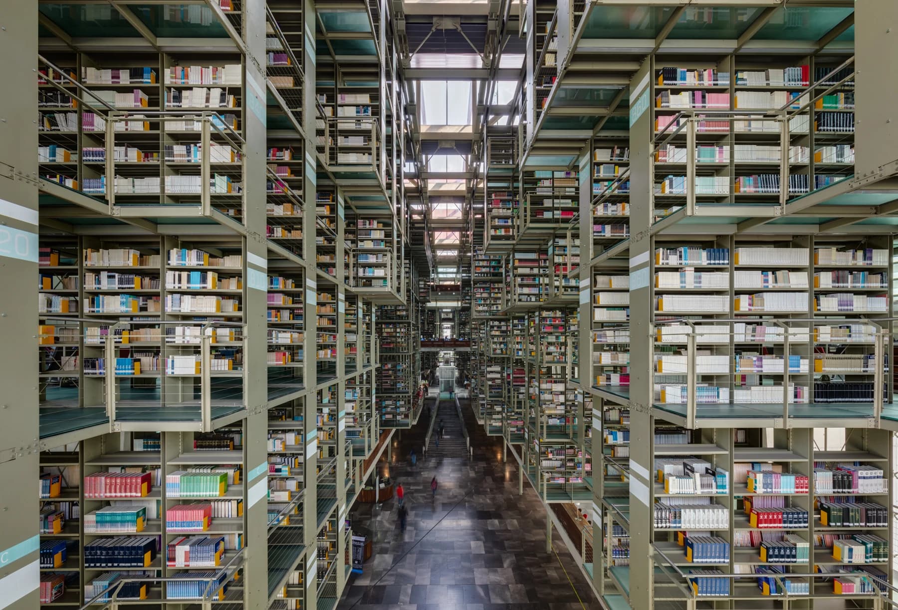 Suspended bookshelves and walkways inside Biblioteca Vasconcelos in Mexico City, seen along a deep central axis with readers on the floor below.