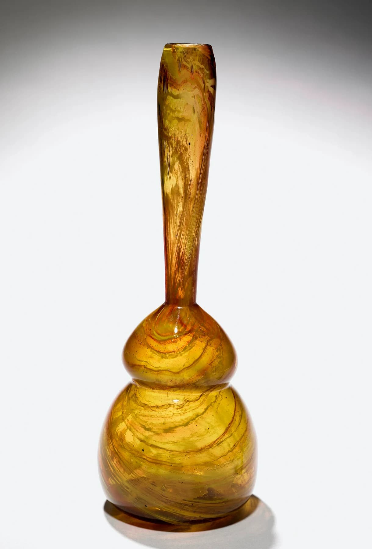 An amber and green Clutha glass vase with a long narrow neck and rounded double-lobed body against a neutral background.