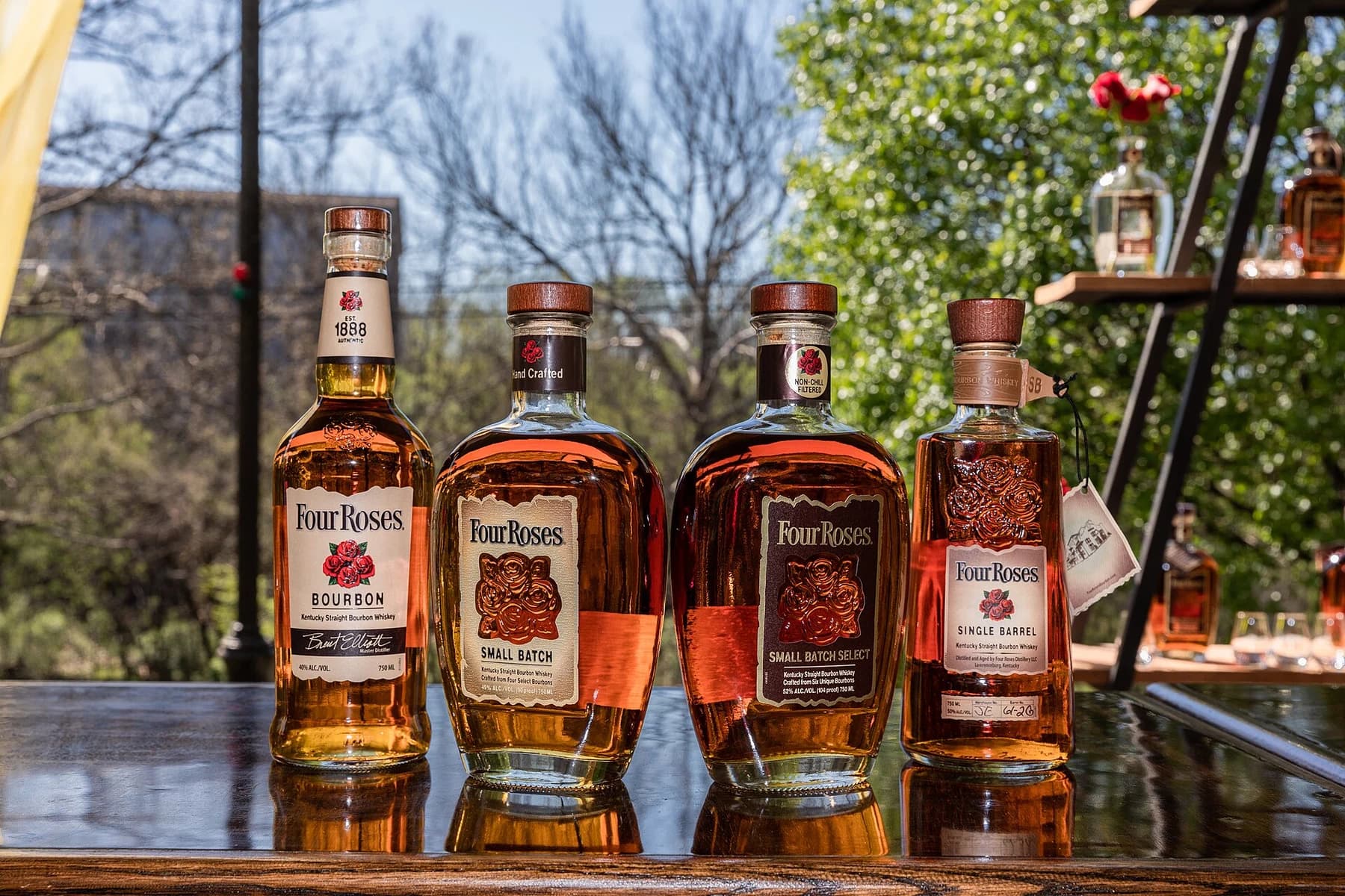 Four Four Roses bourbon expressions on a wooden table outdoors, with Small Batch Select third from the left.