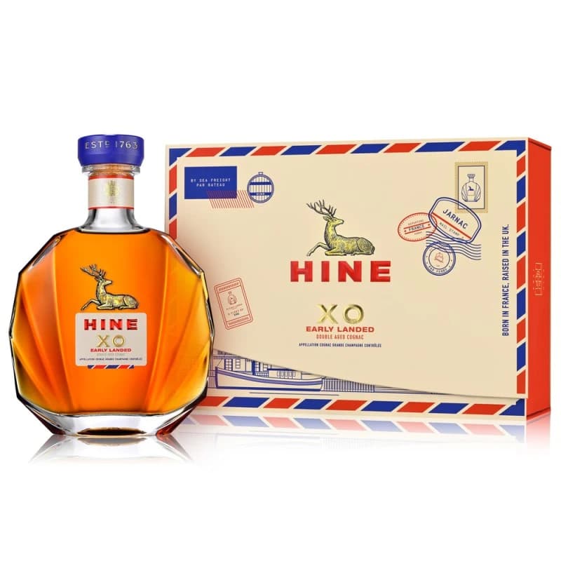 A Hine XO Early Landed cognac decanter beside its cream, red and blue travel-inspired presentation box.