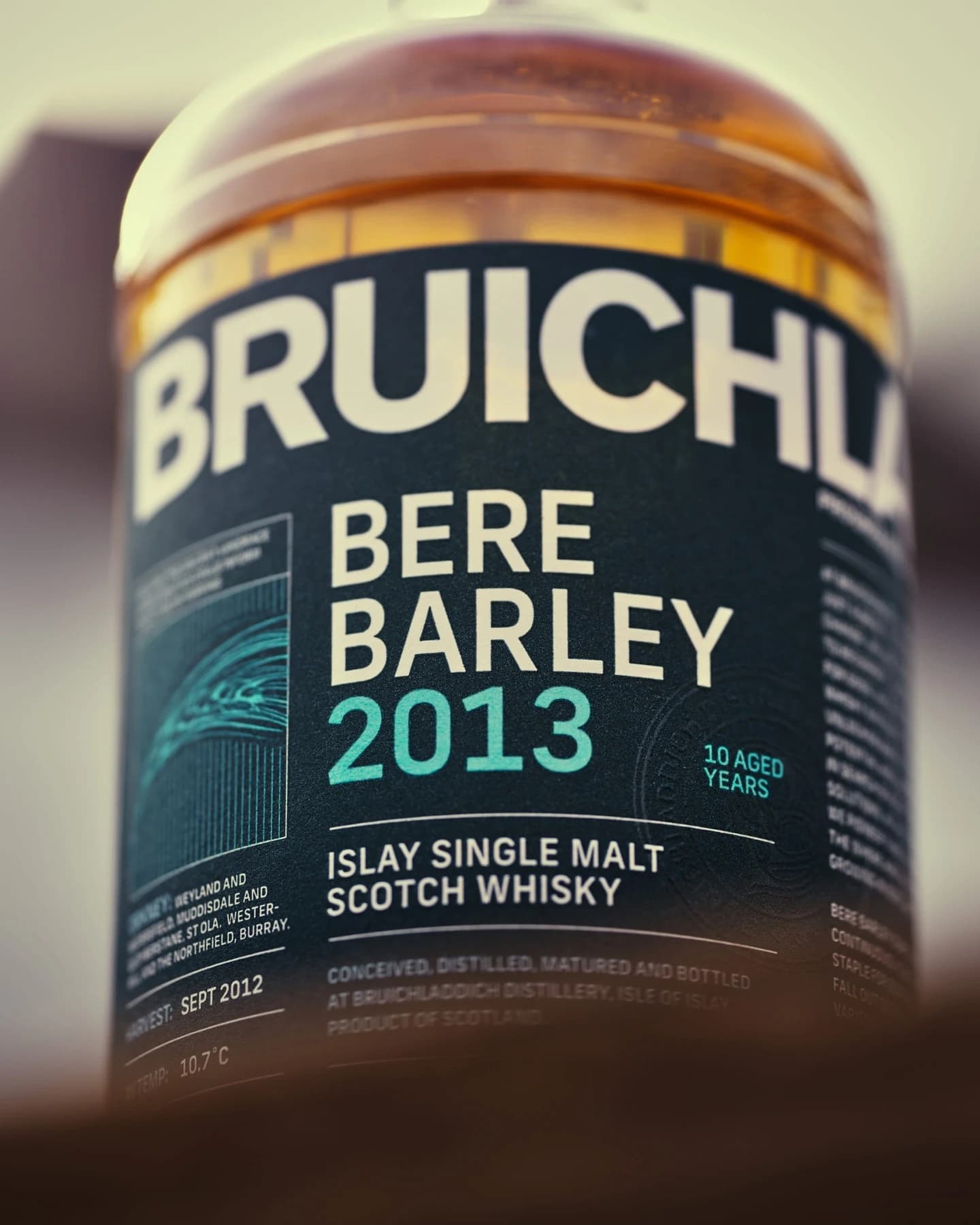 A close photographic detail of the turquoise Bruichladdich Bere Barley 2013 whisky label with ten years of age and fifty percent alcohol visible through the amber bottle.