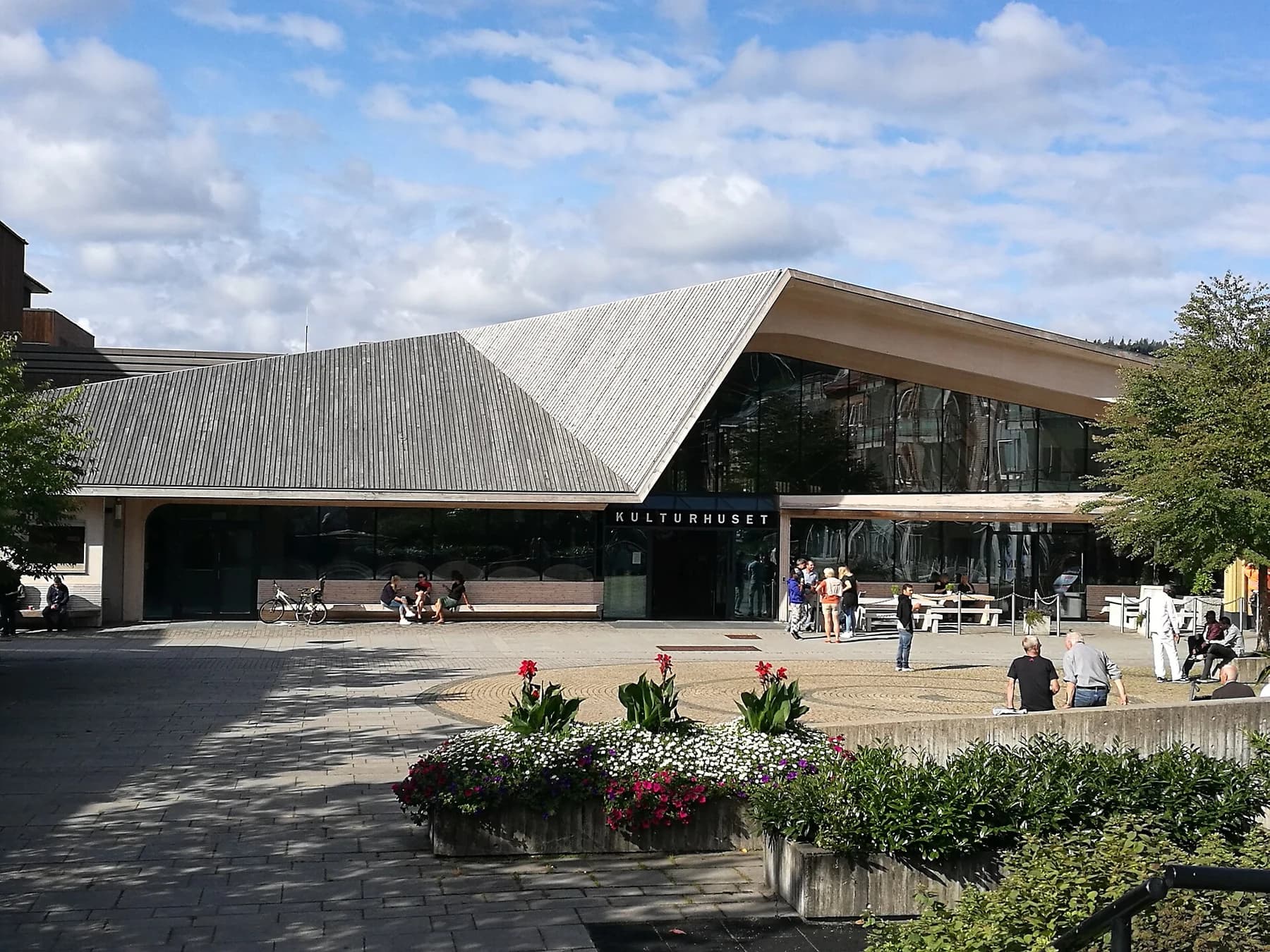 Vennesla Library and Culture House with its angular timber roof, glazed entrance and public square beneath a blue sky.