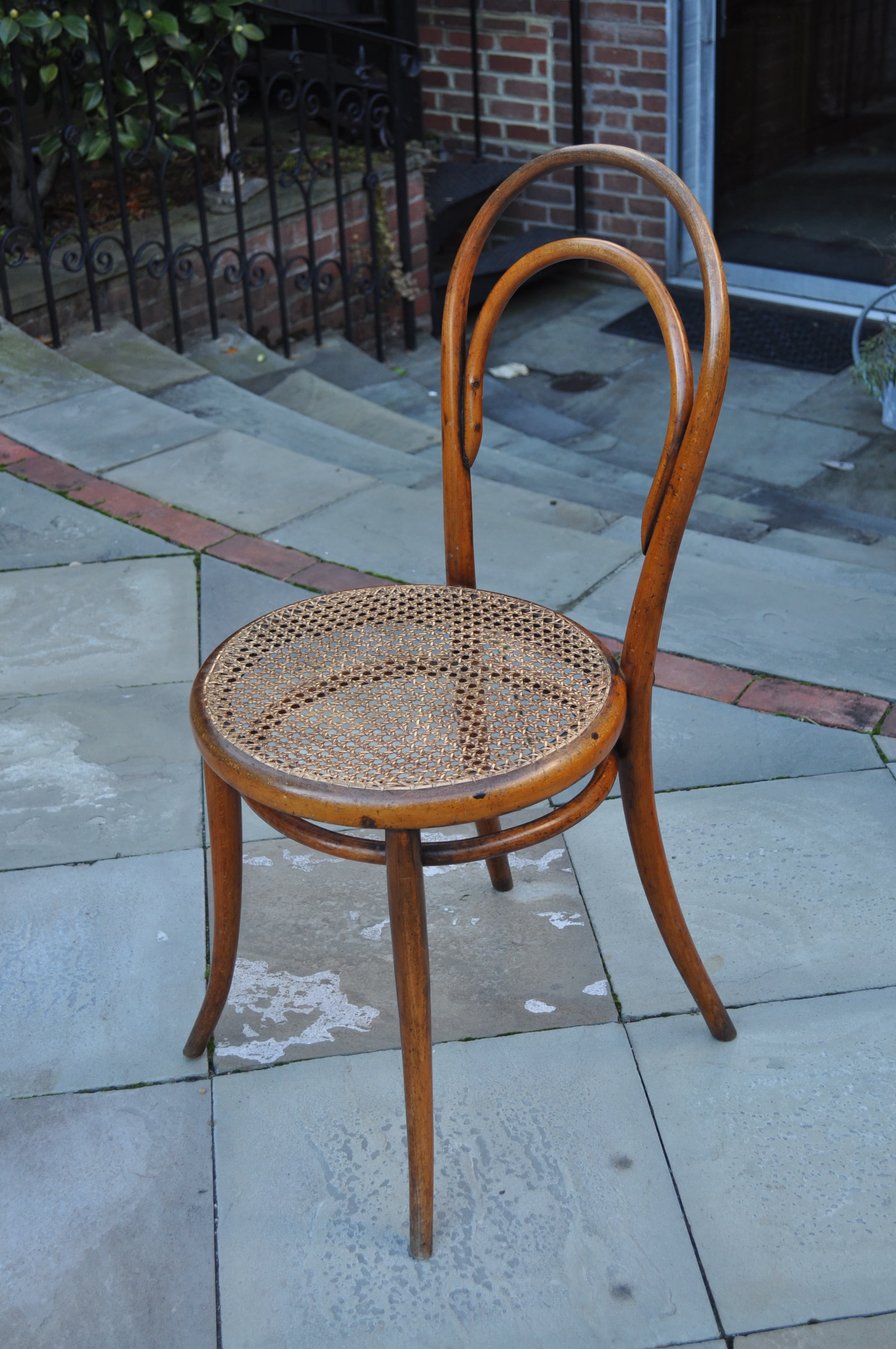A worn Thonet No. 14 bentwood chair with a woven cane seat, photographed on a paved terrace.